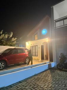 普禾加多patangpuluh homestay的一名男子走过停在房子前的一辆红色汽车。