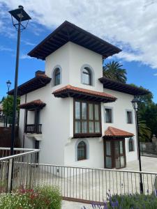 een wit huis met ramen en een hek bij Apartamentos Turísticos La Pontificia in Comillas