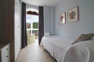 ein weißes Schlafzimmer mit einem Bett und einem Fenster in der Unterkunft Apartamentos Turísticos La Pontificia in Comillas