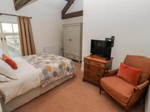 a bedroom with a bed and a tv and a chair at Watermill Cottage in Chathill