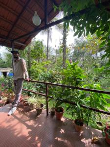 un homme debout sur un porche avec des plantes dans l'établissement Coorg jungle Cottage, à Kushalanagar