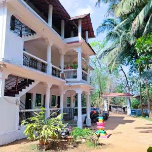 a white house with a balcony and a palm tree at Private Spacious family 1 Bhk Apartment in Arambol in Jāmb