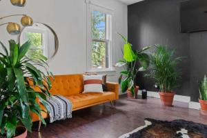 eine orangefarbene Couch in einem Wohnzimmer mit Topfpflanzen in der Unterkunft Jungle House Chillicothe Sleeps 24 Downtown Ohio Free Parking - Walk to Historic District - 5BR Luxury Home - Pet Friendly - King Beds - Over 5,800 Five Star Stays in Chillicothe