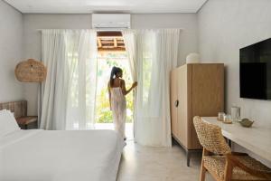 a woman in a white dress looking out of a window at Vila Almesca in Caraíva +51 photos
