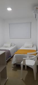 a white room with two beds and a chair at Hostal del Sol Rosario in Rosario