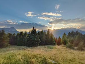 een zonsondergang boven een veld met bomen en bergen bij das Alpenblick & Outdoor Lodge Nauders in Nauders
