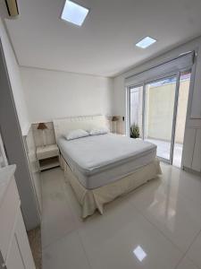 ein weißes Schlafzimmer mit einem Bett und einem großen Fenster in der Unterkunft Casa Riviera Prime in Colônia de Férias