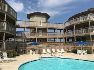 a large apartment building with a pool and chairs and umbrellas at Salty Sisters in Kill Devil Hills