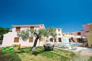 una casa con un patio con un árbol y sillas en Residence con piscina a Sos Alinos, en Cala Liberotto