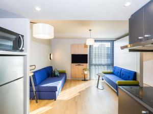 a living room with blue couches and a kitchen at Aparthotel Adagio access Palaiseau Saclay in Palaiseau