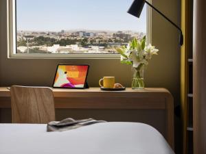 a room with a desk with a laptop and a vase of flowers at Ibis Jeddah Malik Road in Jeddah
