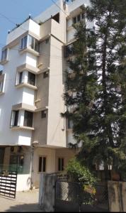 un edificio blanco alto con un árbol delante de él en Homely, Secured, Privacy at Prime Location, en Vadodara