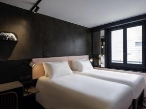 two white beds in a room with a window at TRIBE Paris Batignolles in Paris