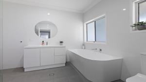 een witte badkamer met een bad en een wastafel bij 30 Curlew Avenue Hawks Nest in Hawks Nest