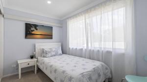 een witte slaapkamer met een bed en een raam bij 30 Curlew Avenue Hawks Nest in Hawks Nest +11 foto's