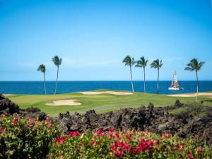a golf course with palm trees and a sailboat in the ocean at Mauna Lani Point in Waikoloa