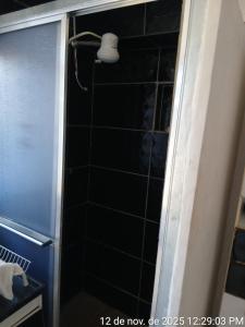 eine Dusche mit schwarz gefliester Wand und einer Lampe in der Unterkunft Kitnet Micro Sobrado in Telêmaco Borba