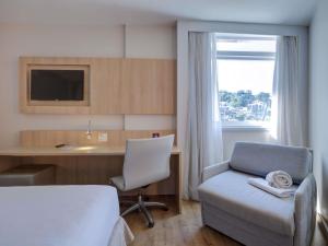 リオデジャネイロにあるMercure Rio de Janeiro Barra da Tijucaのベッドと机と椅子のある寝室