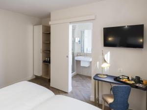 ein Hotelzimmer mit einem Bett und einem Schreibtisch mit einem Fernseher in der Unterkunft Mercure Paris Opera Lafayette in Paris