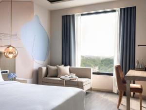 a bedroom with a bed and a couch and a window at Novotel Chandigarh Tribune Chowk in Chandīgarh