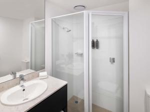 Un baño blanco con ducha y lavabo. en Mercure Sydney Bankstown, en Bankstown