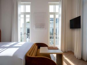 a bedroom with a bed and a table and windows at Elkonin Tel Aviv - MGallery Hotel Collection in Tel Aviv