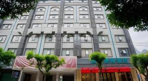 een hoog wit gebouw met bomen ervoor bij City Comfort Inn Hechi Tian'E Bus Terminal in Nandan