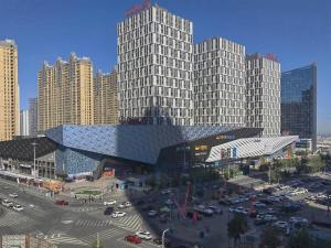 a large building with a parking lot in a city at Xana Hotelle· Wulumuqi High Speed Railway Station Baonengcheng in Ürümqi