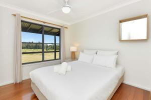 a white bedroom with a large bed and a window at Stay at Shiraz in Pokolbin