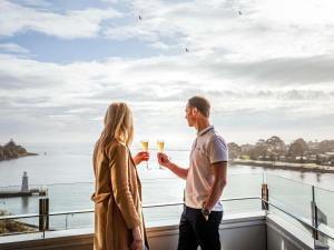 Um homem e uma mulher a segurar taças de champanhe numa varanda. em Novotel Devonport em Devonport