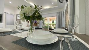 Двухкомнатный дом на Бангтао ДИН في Ban Thalat Choeng Thale: طاولة طعام مع أطباق بيضاء و إناء من الزهور