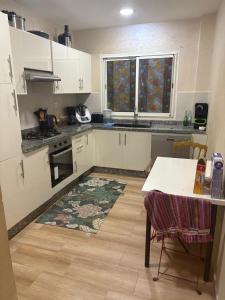 une cuisine avec des armoires blanches, une table et un tapis dans l'établissement Nice apartment with terrace overlooking pool, à Benslimane