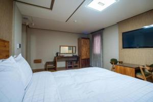 a bedroom with a large white bed and a desk at Jeju Maple Hotel in Jeju