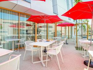 ein Restaurant mit Tischen und Stühlen mit roten Sonnenschirmen in der Unterkunft greet hotel Salon de Provence in Salon-de-Provence