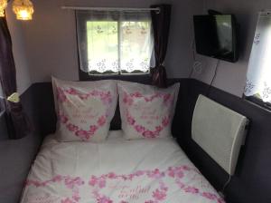 ein Bett mit rosa und weißen Kissen und einem Fenster in der Unterkunft Les Roulottes des Songes de l'Authie in Boufflers