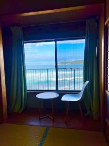 a room with a large window with a table and chairs at コンドミニアム海のまんまえ荘 in Ōda