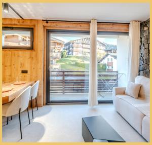 un soggiorno con divano, tavolo e ampia finestra di L'Élégance Alpine I Centre Les Gets a Les Gets