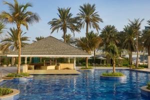 a resort swimming pool with palm trees in the background at Beach Rotana - Abu Dhabi in Abu Dhabi