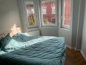 an unmade bed in a bedroom with two windows at Loft industriel - hyper centre cambrai in Salles-sur-Mer