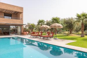 a swimming pool with chairs and umbrellas next to a house at Modern villa - 4 luxury suites - Golf Amelkis - Marrakech in Marrakech