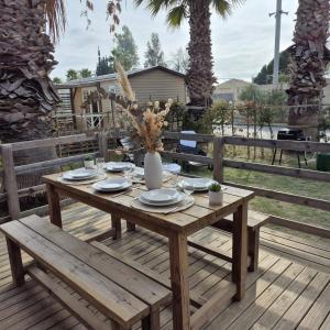 a wooden table with plates and a vase on it at La Palmeraie Mobil Home à 200m de la Plage Camping 5 étoiles Parc Aquatique in Torreilles +23 photos