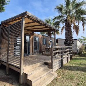 a wooden cabin with a deck and a palm tree at La Palmeraie Mobil Home à 200m de la Plage Camping 5 étoiles Parc Aquatique in Torreilles