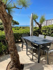 a table with chairs and a surfboard next to a tree at Le Cosy - T4 avec terrasse privée, Face à la mer avec parking et wifi in Sète
