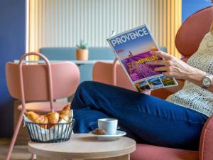 a woman sitting on a couch reading a magazine at Novotel Aix-en-Provence Pont de L'Arc in Aix-en-Provence