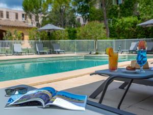 a table with a book and glasses next to a pool at Novotel Aix-en-Provence Pont de L'Arc in Aix-en-Provence