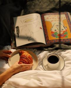第比利斯Artifact Apart Hotel的一个人一边看书，一边吃着一盘食物，喝着一杯咖啡。