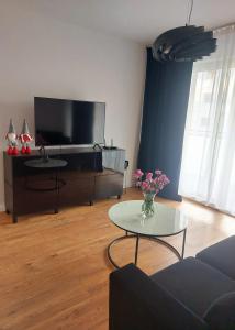 a living room with a tv and a table with flowers at Apartament 24 Bolesławiec z garażem podziemnym in Bolesławiec
