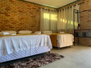 a bedroom with two beds and a brick wall at Pousada Flor do Café in Ubajara