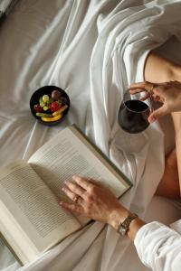 a woman laying in bed holding a book and a cup of wine at Puro Dão Hotel & Spa in Nelas