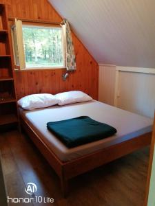 Bett in einem kleinen Zimmer mit Fenster in der Unterkunft Les chalets au bord de l'étang de Malleteix in Champagnat